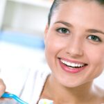 Smiling woman brushing her teeth with a blue toothbrush in a bright bathroom