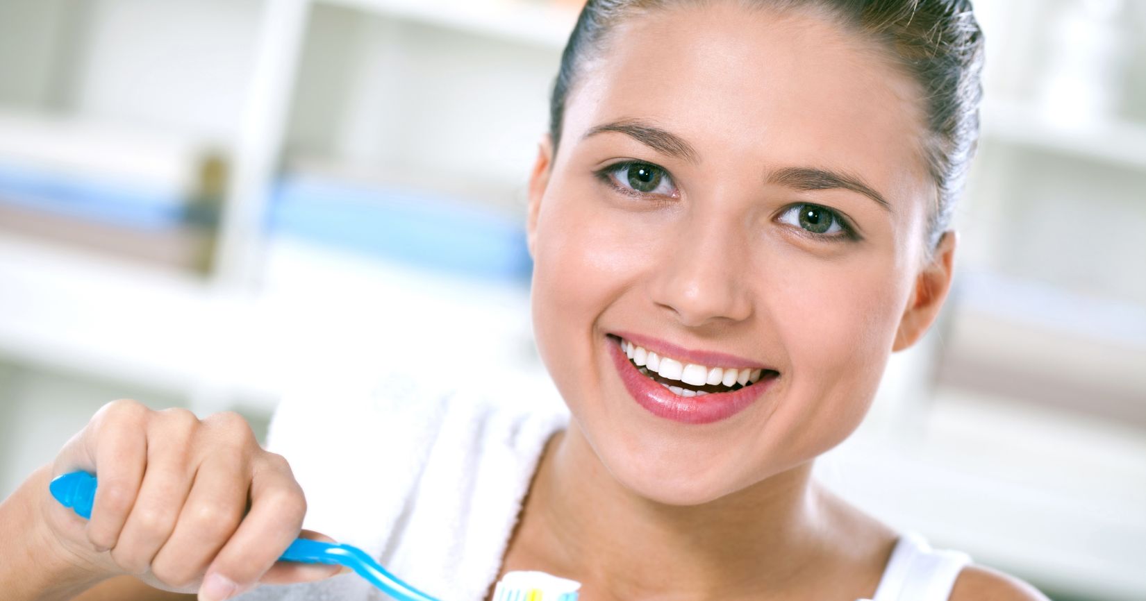Smiling woman brushing her teeth with a blue toothbrush in a bright bathroom