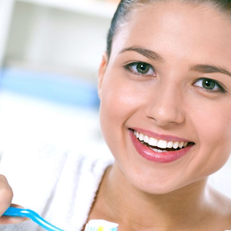 Smiling woman brushing her teeth with a blue toothbrush in a bright bathroom